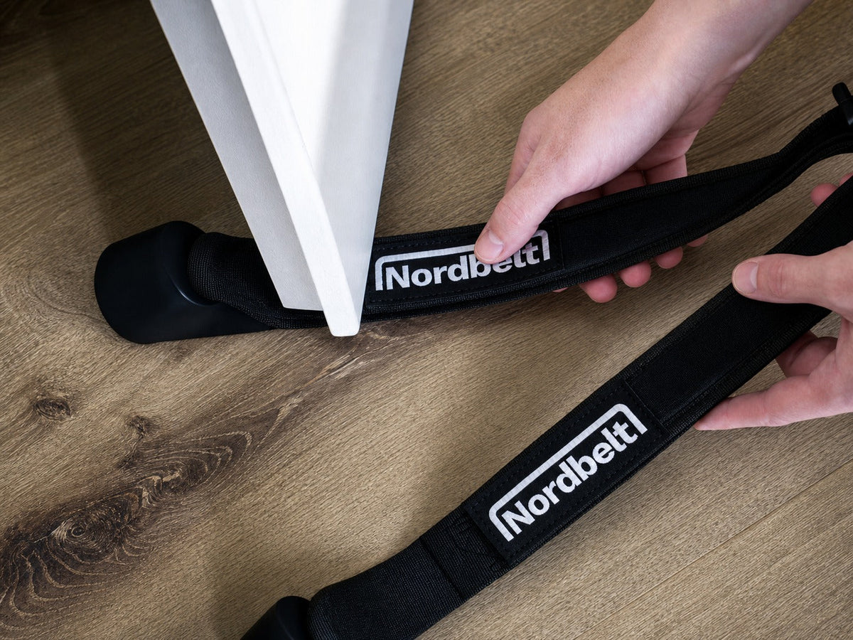 Handen plaatsen de ankerdelen van twee Nordbelt-banden onder een open witte deur.