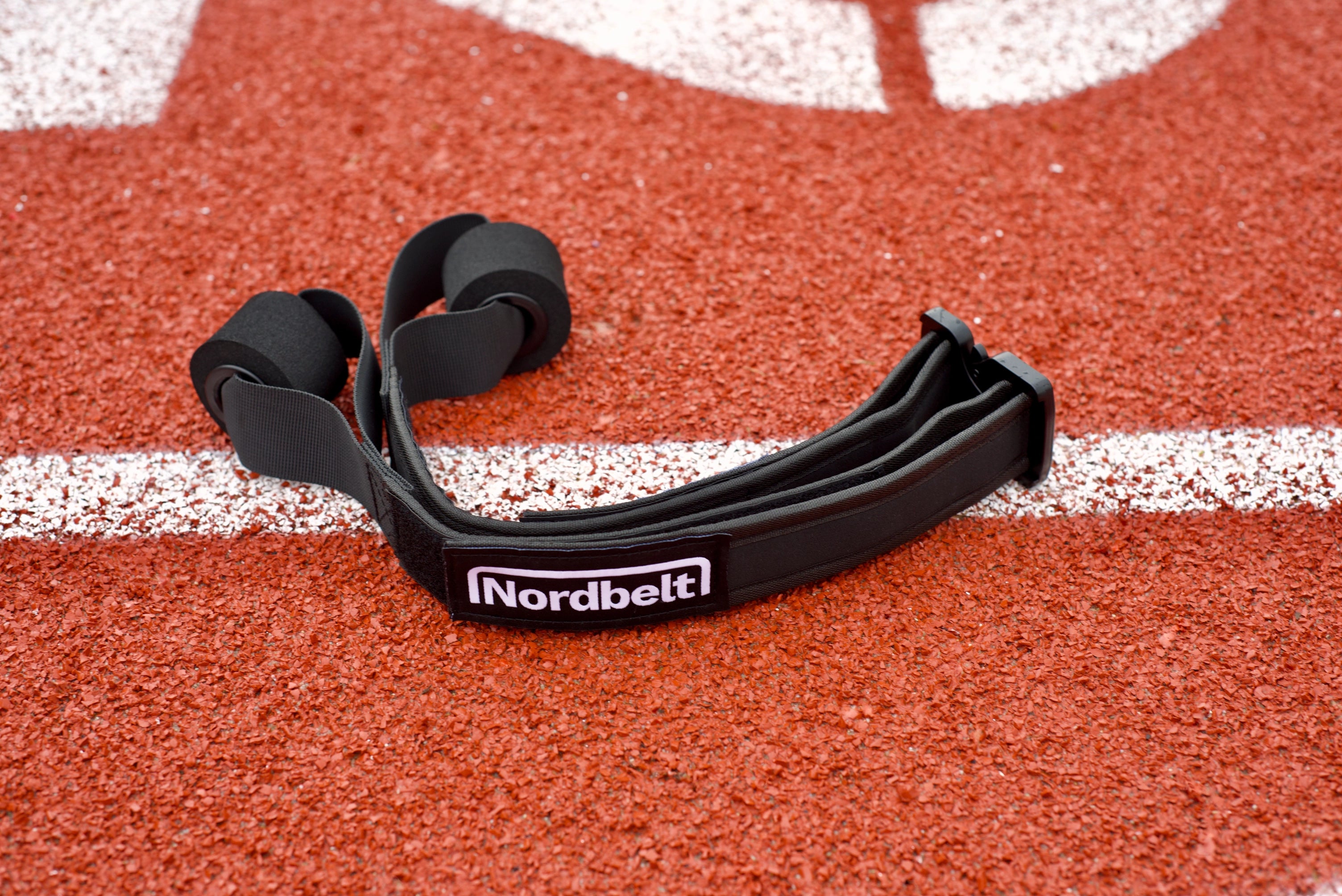 Nordbelt on a red running track with black ankle strap, round slider pad and carry bag.